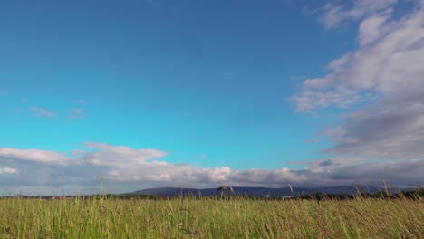 timelapse-of-clouds-passing-over-a-field-with-blue-sky-and-mountains
