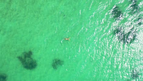 Young-woman-swimming-on-shallow-turquoise-lagoon-near-tropical-island-coastline,-reflecting-sunshine-in-Bermuda