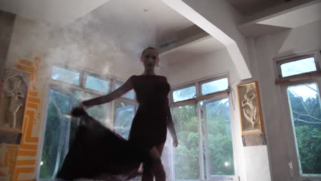 A-mysterious-young-woman-with-shaved-head-is-holding-a-smoke-grenade-and-dancing-dramatically-back-and-forth-barefoot-while-spreading-the-smoke-around-the-room