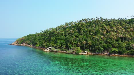 Palm-trees-forest-on-tropical-island's-hill-with-rocky-shoreline-surrounded-by-green-turquoise-sea-water-in-Philippines