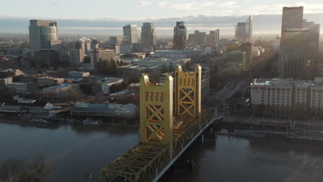 Aerial-drone-tilt-up-of-Tower-Bridge-and-Downtown-Sacramento,-CA,-including-Old-Sacramento---State-Capitol-in-background-during-sunrise