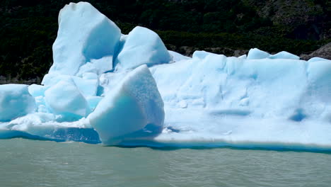 Sunlit-Melting-Iceberg-Floating-Along-Grey-Lake,-Pan-Left