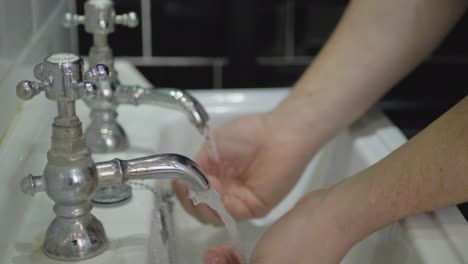 Der-Mann-Wäscht-Sich-Die-Hände-Im-Waschbecken-Mit-Zwei-Separaten-Warm--Und-Kaltwasserhähnen