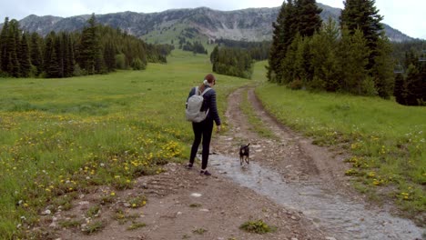 Mujer-Caminando-Con-Un-Pequeño-Perro-Negro-En-Un-Camino-De-Tierra-En-Las-Montañas