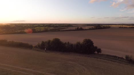 Slowly-descending-down-towards-a-harvested-field-while-looking-out-over-a-summer-sunset-1