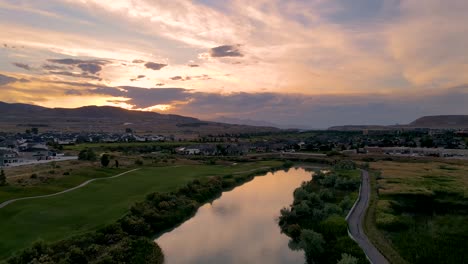 Fliegen-Sie-Bei-Sonnenuntergang-über-Einem-Fluss-Und-Einem-Golfplatz,-Wobei-Der-Farbenfrohe-Himmel-Von-Der-Oberfläche-Des-Flusses-Reflektiert-Wird