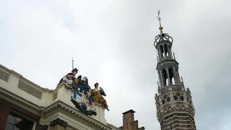 Static-shot-showing-holy-statues-on-building-beside-church-tower-against-cloudy-sky-in-Alkmaar
