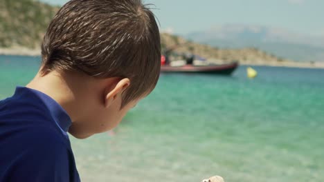 Close-up-of-caucasian-boy,-eating-a-snack-at-the-beach-with-blurry-background-120fps