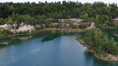 Aerial-View-of-lake-with-Beautiful-Water-in-a-Quarry-Surrounded-by-Forest-Tracking-Backward