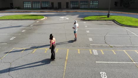 man-and-woman-riding-onewheel-electric-skateboards-through-parking-lot-on-sidewalk-aerial-drone