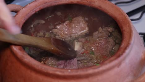 Seasoning-vegetables-and-meat-in-clay-pot-with-wooden-spoon