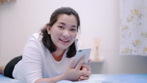 Thai-asian-woman-looking-and-touching-smartphone-relax-enjoy-and-smile-with-online-social-media-in-bedroom