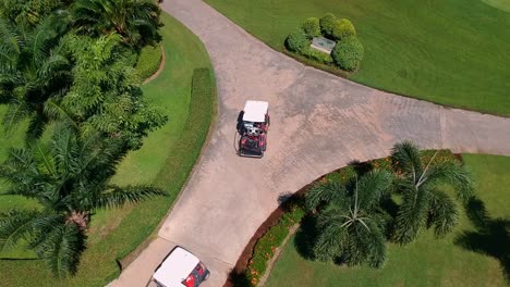 Aerial-top-down-shot-following-two-golf-carts-on-path-between-green-golf-course