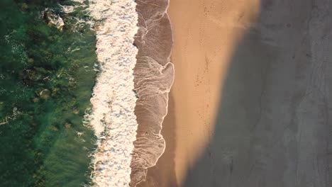 Aerial-top-down-view-of-waves-breaking-on-beach-at-sunset