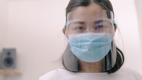 Portrait-of-an-Asia-young-female-who-is-wearing-a-face-shield-with-mask-rounded-around-her-face-from-a-frontal-perspective-to-protect-her-glasses-and-eyes,-scene-of-slow-motion
