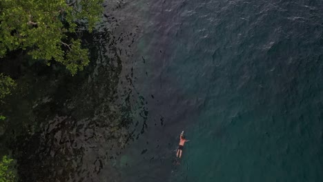 Drone-shot-of-a-young,-white-tourist-swimming-alone-in-the-colorful-water