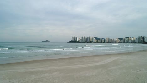 Drone-footage-from-the-beach-sand-towards-the-calm-and-calm-sea,-buildings-in-the-background-and-cloudy-weather,-Brazil-beach,-Guaruj?
