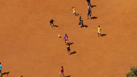 Niños-Africanos-Juegan-Al-Fútbol-Juntos-En-Tierra-Roja-Brillante-En-Super-Cámara-Lenta