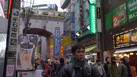 Street-level-view-of-sbusy-street-in-Akihabara,-Tokyo-with-train-running-on-tracks-above