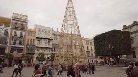 Tilt-Down,-Christmas-tree-made-of-lights-in-busy-downtown-square,-Seville,-Spain
