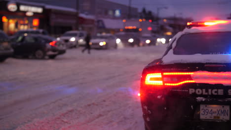 Police-Car-with-Lights-on,-blocking-road-while-cars-drive-through-snow
