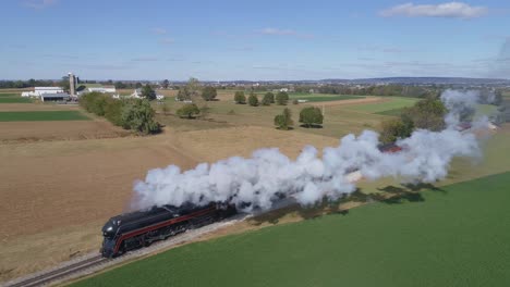 Aerial-view-of-a-steam-train-blowing-smoke-and-steam-while-traveling-along-countryside-followed-from-ahead-of-train