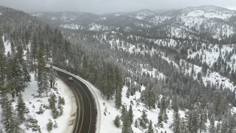 Aerial-shot-of-a-car-driving-on-a-road-surrounded-by-woods-and-revealing-a-snowy-winter-landscape