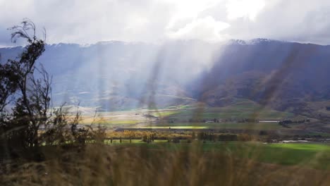 Slow-reveal-of-mountainous-valley-with-sun-rays-beaming-through-and-foreground-plants