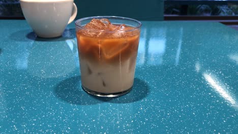 Glass-of-Cold-Brew-and-Milk-in-Separated-Layers-With-Ice-Cubes-on-a-Turquoise-Table