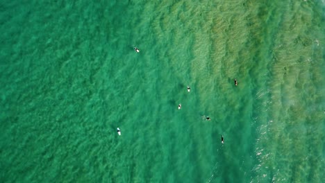 Drone-aerial-pan-shot-of-Pacific-ocean-with-surfers-waiting-for-swell-waves-on-sandbar-North-Avoca-Beach-NSW-Australia-4K
