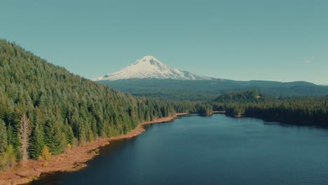 4k-aerial-snowy-mountain-with-lake-and-evergreen-hills-in-foreground-drone-truck-right