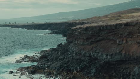 4k-Aerial-volcanic-cliff-on-calm-ocean-Drone-ib-down-+-dolly-in-shot