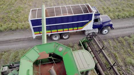 AERIAL---Combine-harvester-throws-grain-onto-a-truck,-wide-spinning-shot