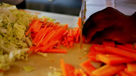 A-African-American-chef-chopping-up-carrots-with-a-meat-clever-in-slow-motion,-static-shot