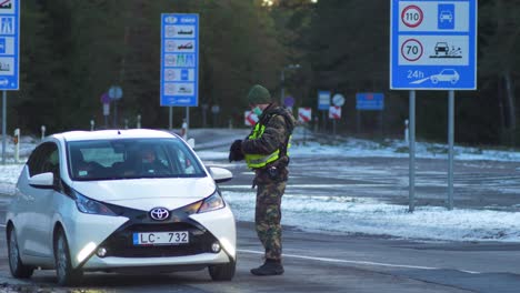 Lithuanian-border-guard-officer-control-white-passenger-car-at-the-Lithuania---Latvia-border-during-crisis-measures-in-the-fight-against-the-novel-coronavirus-Covid-19,-medium-shot-from-a-distance