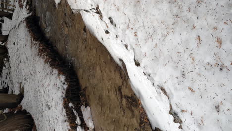 Vertical-Video,-Fresh-Water-Creek-Rushing-on-Cold,-Snowy-Winter-Hike-Path