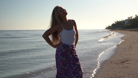 Pretty,-mature,-backlit-woman-on-a-beach-looks-away-from-the-sea-and-then-raises-her-arms-and-smiles-looking-to-the-sky