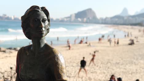 Bronzestatue-Von-Clarice-Lispector,-Einer-Ukrainischen-Journalistin-Und-Schriftstellerin,-Geboren-1920-Und-Eingebürgerte-Brasilianerin-Mit-Menschen,-Die-Im-Hintergrund-Am-Copacabana-strand-Freizeitaktivitäten-Ausüben