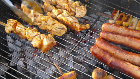 Grilling-Sausages-And-Marinated-Chicken-On-The-Barbeque-Griller-And-Turning-Using-Tongs-Over-Charcoal