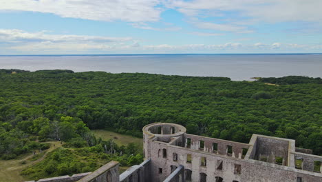 Drone-Flying-Over-The-Ancient-Borgholm-Castle-Ruin-In-Oland,-Sweden-With-Lush-Trees-At-The-Coast-Of-Baltic-Sea---aerial