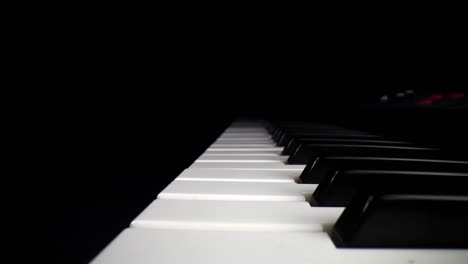 Low-profile-wide-angle-macro-of-electronic-keyboard---moving-backwards-aligned-in-the-middle-of-the-white-keys,-as-the-song-assist-lights-the-keys-a-red-glow-near-far-end-of-keyboard