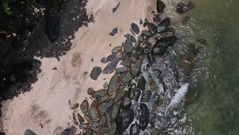 Drone-vertical-tracking-and-tilt-shot-of-jungle-beach-and-rocky-coastline-with-waves-crashing-on-the-shoreline
