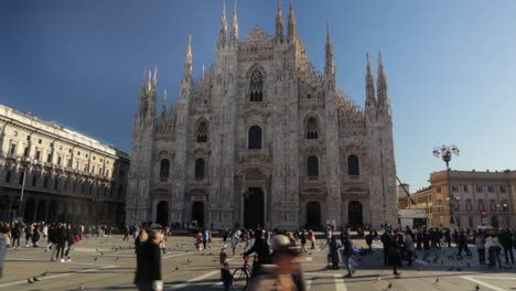 Duomo-di-minalo-cathedral-front-view-with-the-plazza-filed-with-tourists,-truck-left-wide-shot-in-Milan-during-bright-sunny-day
