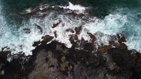 Rising-downward-view-of-a-volcanic-coastline-with-the-waves-crashing-into-the-rocks