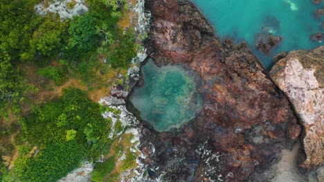 Aerial:-top-down-view-of-rock-pool-on-small-island-surrounded-by-turquoise-water