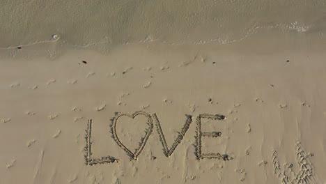 Liebe,-Die-Sich-An-Einem-Strand-In-Den-Sand-Eingeschrieben-Hat-Und-Den-Rahmen-Ausfüllt-Und-Mit-Der-Zeit-Kleiner-Wird