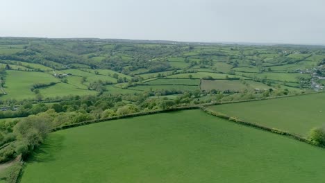 Aerial-over-a-plateau-ridge-to-reveal-a-valley-of-gorgeous-english-countryside,-fields,-trees,-and-rural-homesteads