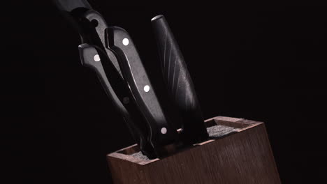 Set-Of-Kitchen-Knives-With-Black-Handle-Placed-On-Wooden-Knife-Holder-Isolated-On-Black-Background---Closeup-Shot