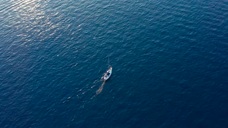 Aerial-top-view-of-small-sailboat-moving-in-blue-sea-on-a-sunny-day
