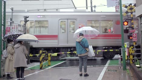 Japaner-Mit-Regenschirmen,-Die-Darauf-Warten,-Dass-Der-Zug-Durchfährt,-Bevor-Sie-An-Einem-Regnerischen-Tag-An-Der-Eisenbahn-In-Tokio,-Japan,-überqueren---Stativ-Slowmo-Nahaufnahme